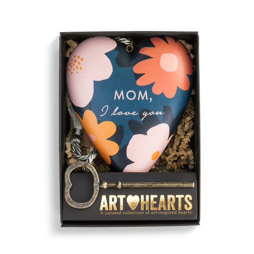 A blue art heart with several pink and orange flowers and reads Mom, I love you" in pink cursive letters. With a bronze key and a silver tassel. Placed in a black packaging box."