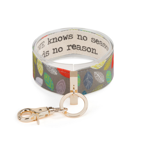 An expanded gray and multi color leaf print wrist strap with gold metal accents. Inside reads "love knows no season and no reason".