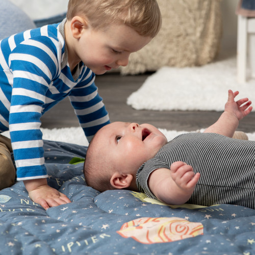 A toddler playing with a baby on a blue space themed play mat.