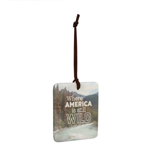 A square tile hanging ornament with a mountain stream and says "Where America is still Wild", displayed angled to the right.