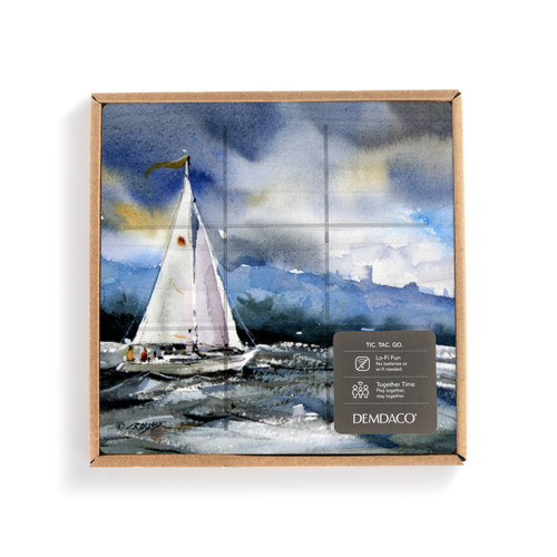 A square wood tic tac toe board with a watercolor image of a sailboat at sea, displayed in a packaging box with a product information tag attached.