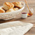 Cream bread basket with rolls inside - next to small jelly jar and honey pot