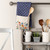 kitchen shelving with mugs, planter and white ceramic crock holding cooking utensils, towel with pocket hanging on rod holding wooden spoon