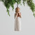 Small girl figurine faceless wearing white dress holding brown book - background is white with green branches on top
