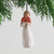 Little girl figurine wearing white dress holding red flower boquet in her arms - green tree branches and white background