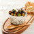 white ceramic bowl with leaf pattern holding olives sitting on wooden cutting board with wooden spoon and bread sitting next to it