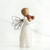 Side view of brunette angel figurine in white dress and black wire wings holding apples