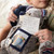 A close up image of a young boy sitting with his army mother, holding a plush gray bear with a note and family picture enclosed.