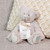 A cream plush birthstone bear with a light green nose and embroidered heart on its foot for the March birthstone of Aquamarine, displayed sitting on a couch.