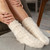 A close up image of a woman sitting on a gray couch with her feet propped up on a gray ottoman. Wearing cream socks.