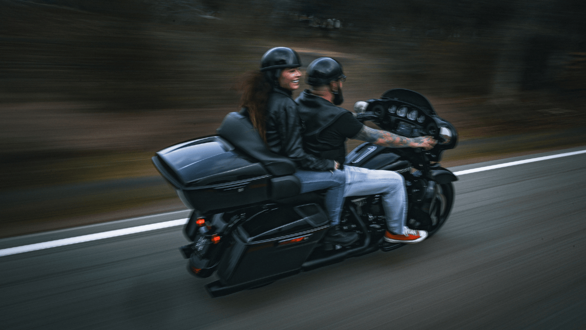 Action shot of couple riding down the street on a Harley Davidson motorcycle.