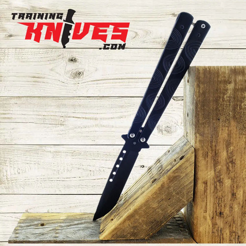 Hero – Black Chrome 440 Steel Balisong Butterfly Trainer open with unsharpened blade, leaning against a tree stump, showcasing black chrome skeletonized handles Hero – Black Chrome 440 Steel Balisong Butterfly Trainer open with unsharpened blade, leaning against a tree stump, showcasing black chrome skeletonized handles