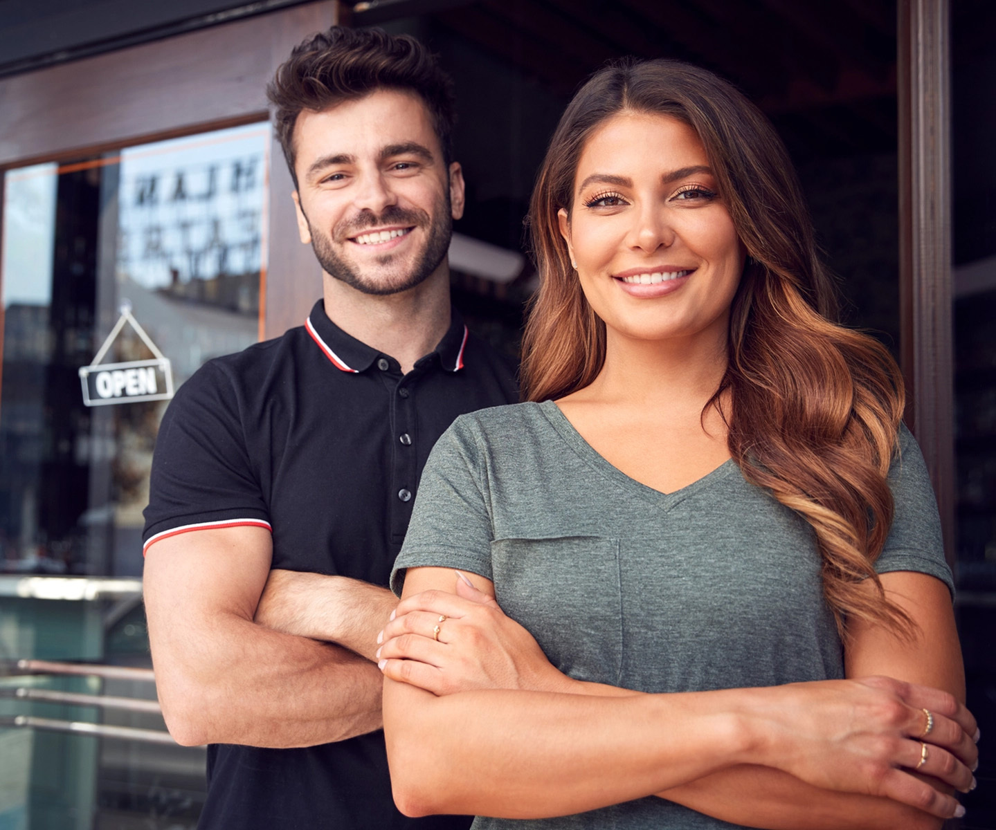 Confident looking man and women standing in front of their store with an open sign