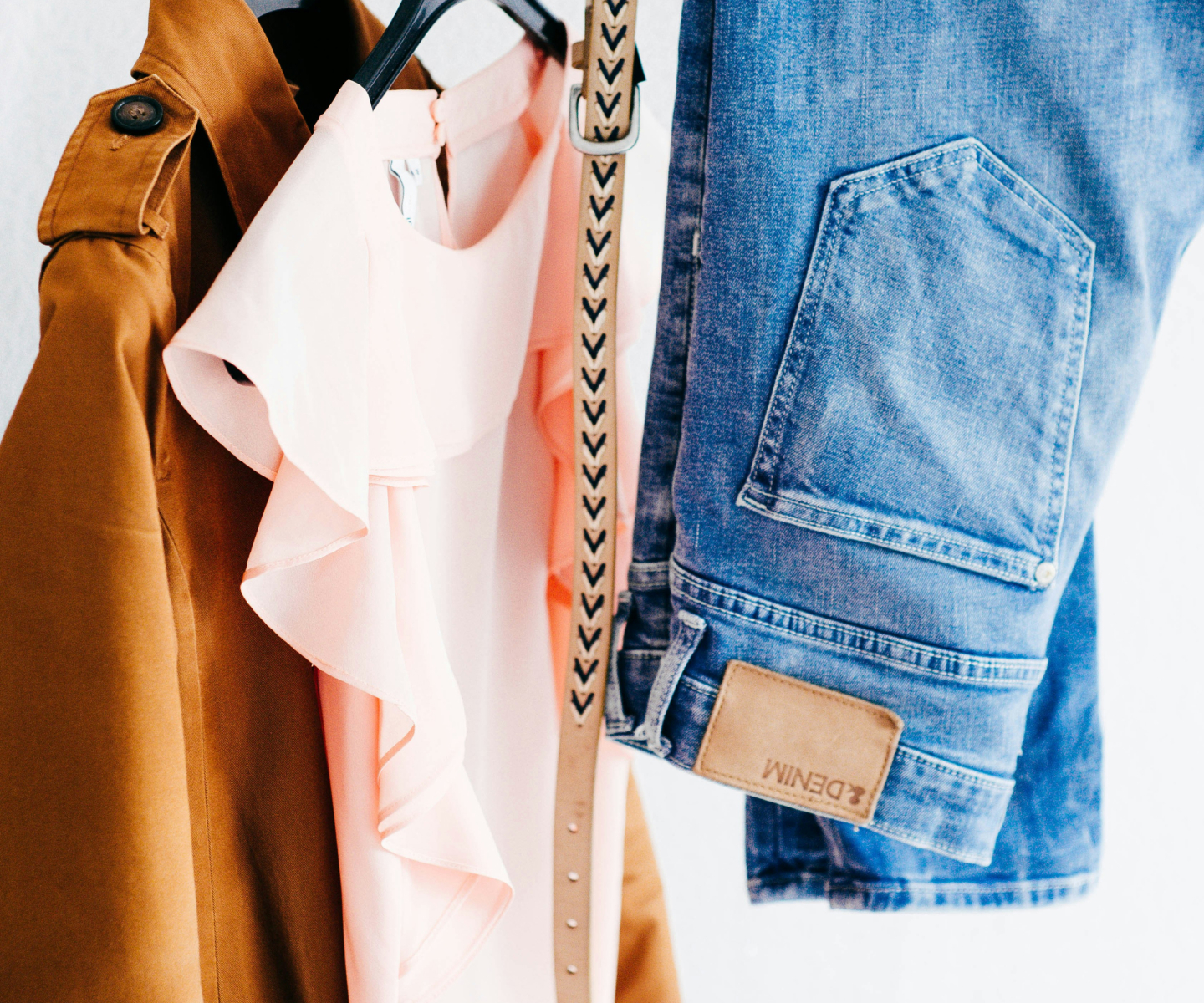 a brown jacket, pink blouse, and pair of jeans hanging on clothing rack