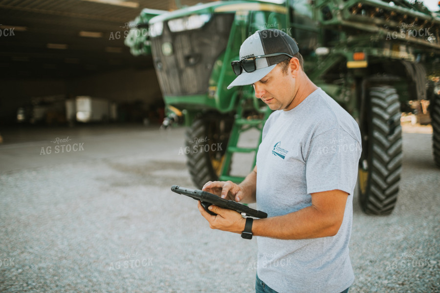 Farmer Looking at iPad with Sprayer in Background 6248