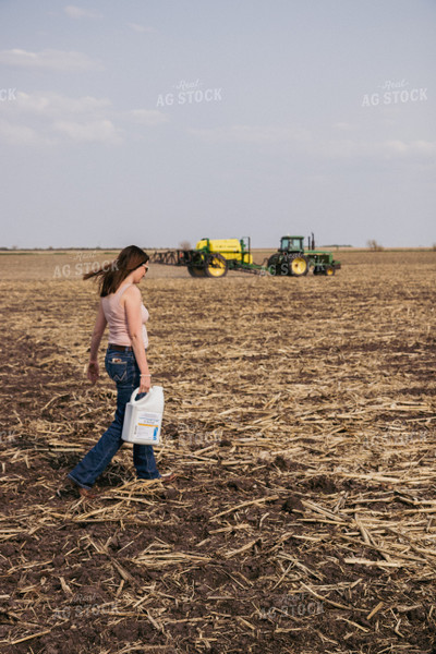 Female Farmer Carries Pesticide Concentrate in Field with Sprayer in Background 67285
