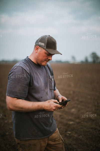 Farmer Looking at Phone in Field with Planter 5672
