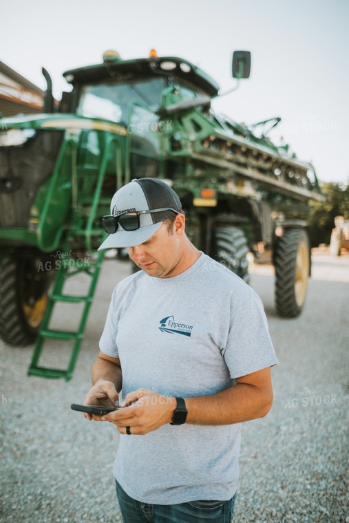 Farmer Looking at Phone with Sprayer in Background 6252