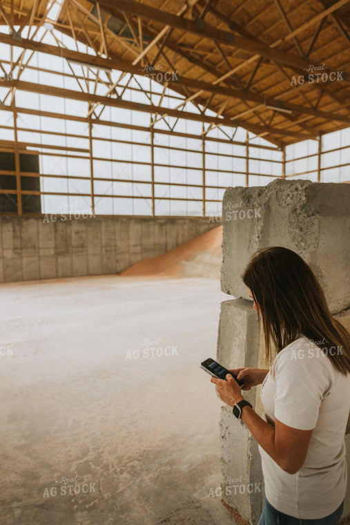 Woman Farmer Looks at Phone in Dry Feed Storage Shed 7536