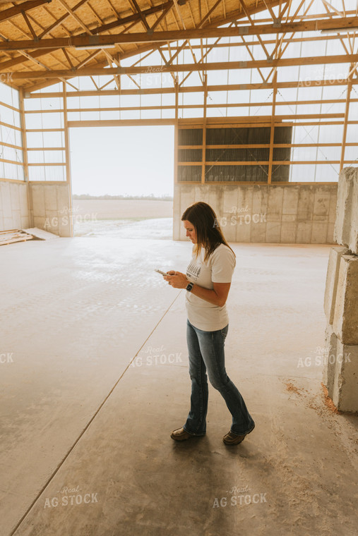 Woman Farmer Looks at Phone in Shed 7537