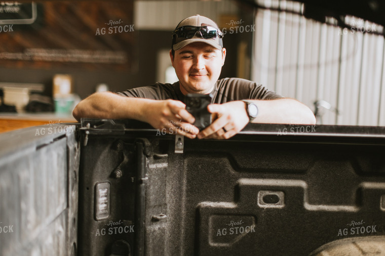 Farmer Looks at Phone While Leaning on Truck Bed 7574