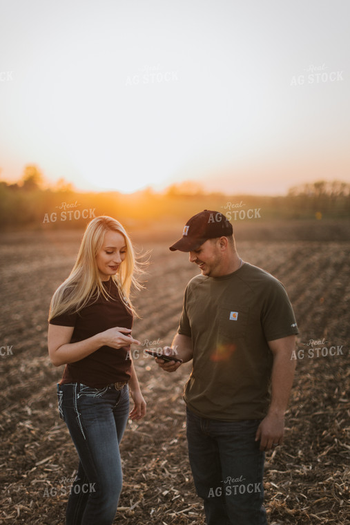 Young Couple Look at Phone in Field at Sunset 7729