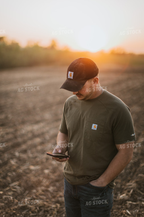 Young Farmer Looks at Phone in Field at Sunset 7730