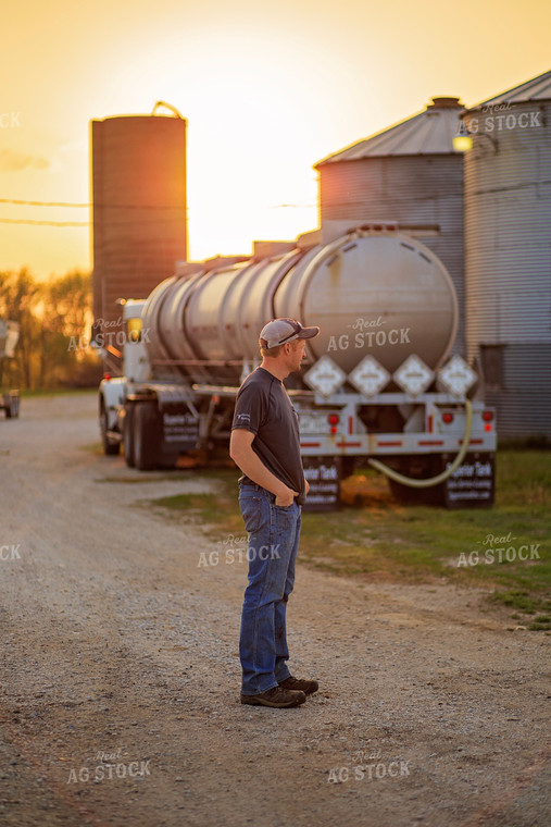 Farmer Stands in Front of Tanker Truck at Sunset 93196