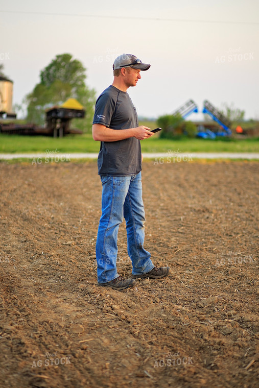 Farmer Looks at Phone in Field 93210
