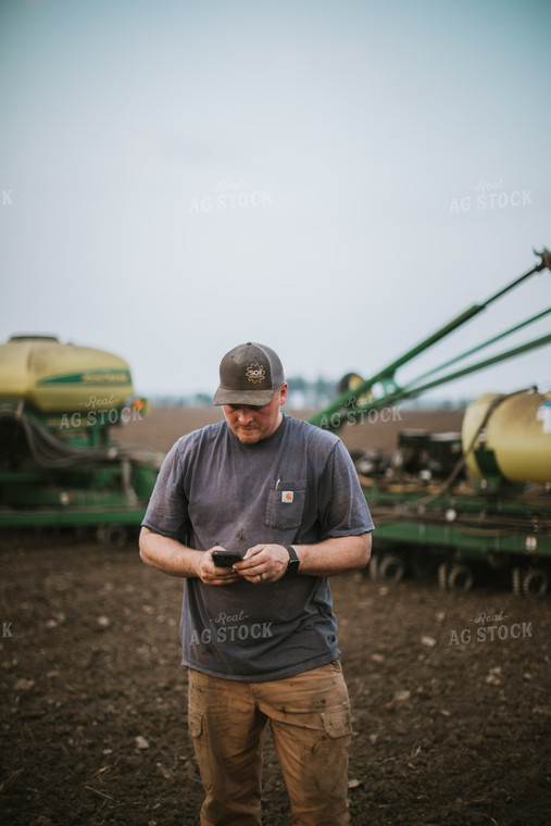 Farmer Looking at Phone in Field with Planter 5674