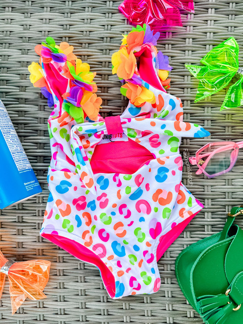 Fashionistots colorful kids' monokini swimsuit. The swimsuit features vibrant floral embellishments along the straps and a playful, multicolored abstract print resembling leopard spots.