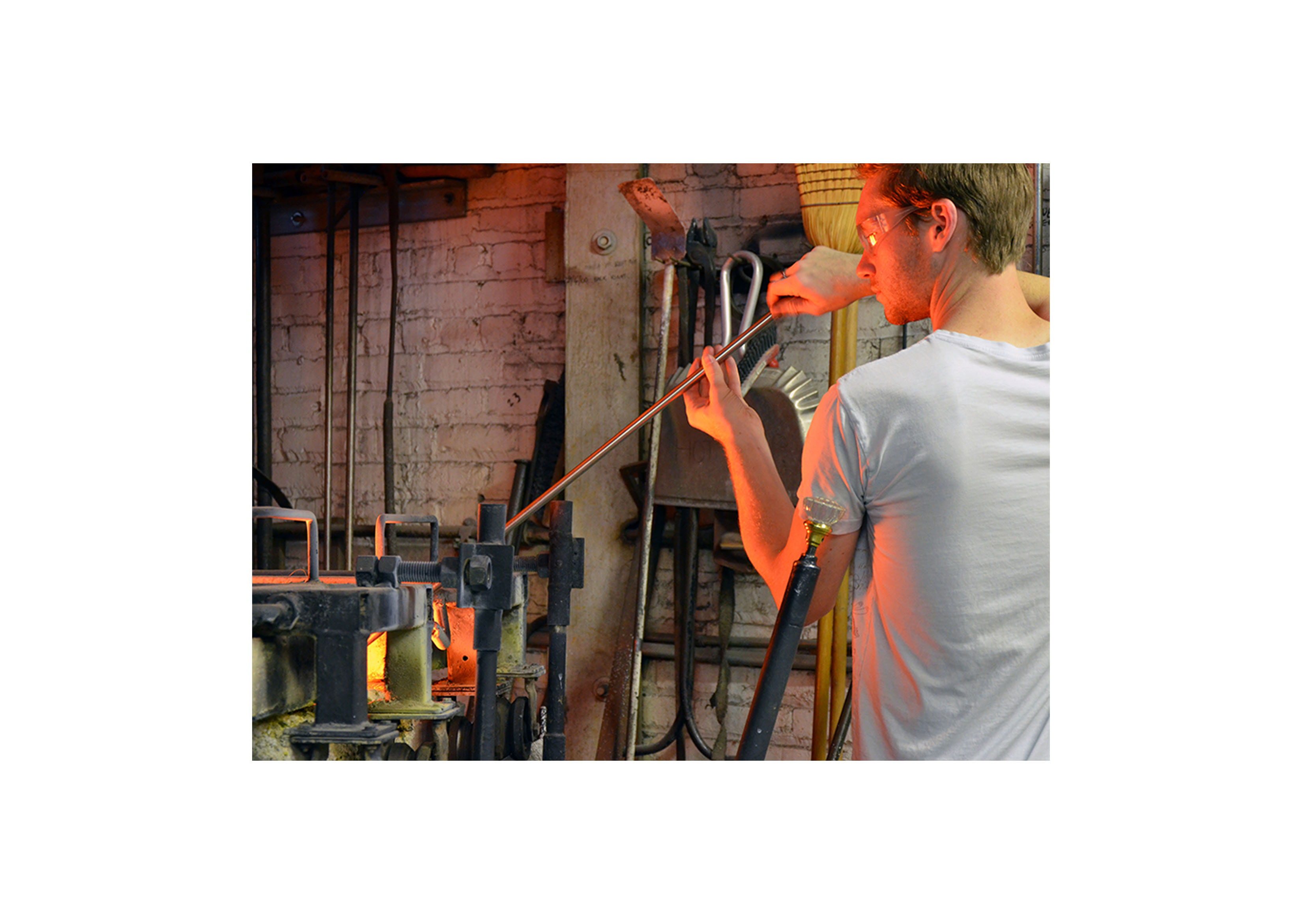 a modern shot of a young man working on a piece of molten blown glass