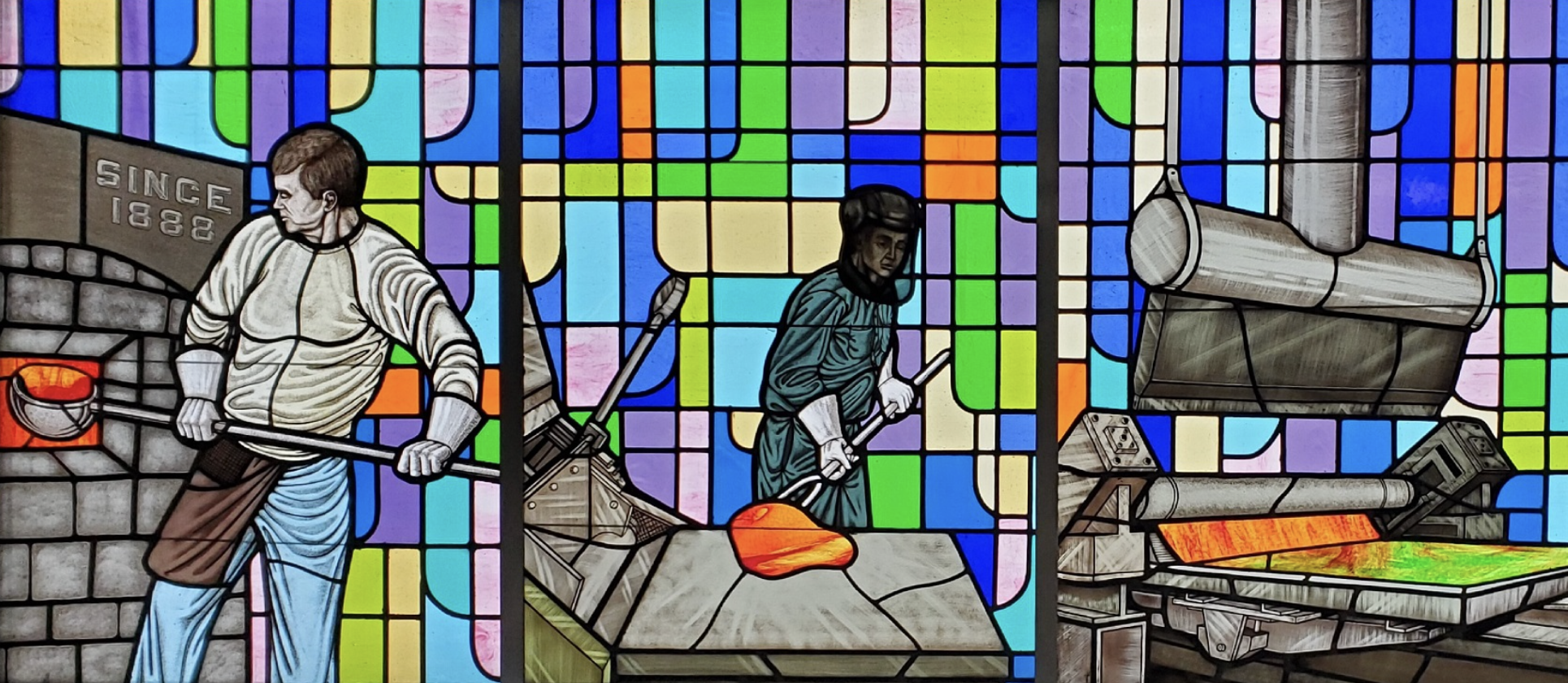 stained glass panels featuring men working with molten glass in the factory