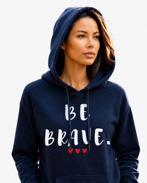 Woman modeling a black motivational hoodie featuring the “BE BRAVE” graphic and three red hearts outdoors in the mountains. Inspirational apparel designed to encourage confidence, empowerment, and self-belief.