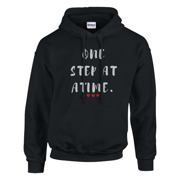 Black pullover hoodie featuring the inspirational phrase “One Step at a Time” in distressed white lettering with three small red hearts beneath. The hoodie includes a drawstring hood, front kangaroo pocket, and classic unisex fit. The encouraging design promotes resilience, hope, and steady progress through life’s challenges.