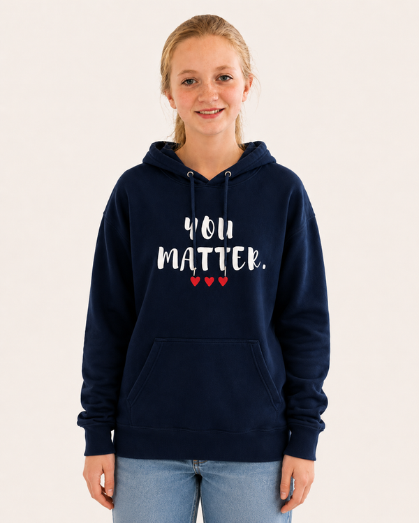 Young girl wearing a navy blue pullover hoodie featuring the uplifting phrase “You Matter” in white distressed lettering with three red hearts beneath. She is holding a bowl of ice cream indoors, creating a warm and positive lifestyle scene. The hoodie includes a drawstring hood, front kangaroo pocket, and relaxed fit, promoting self-worth, encouragement, and kindness.