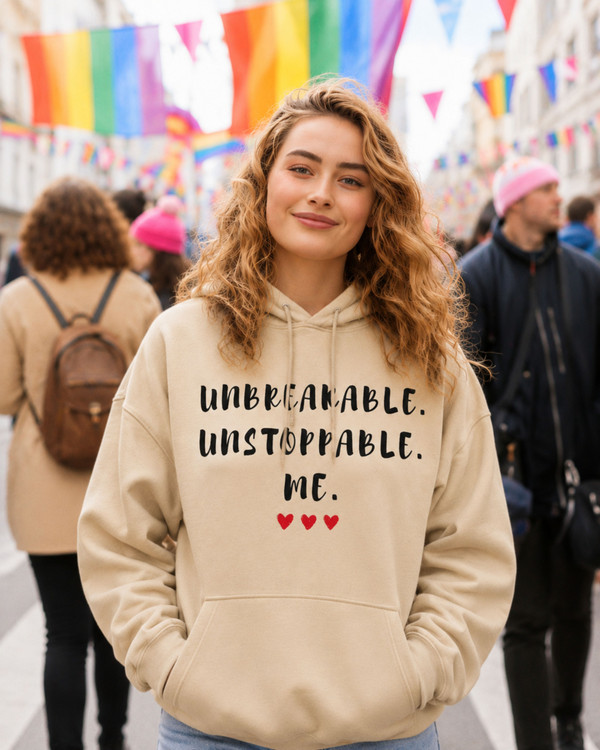 Woman wearing a beige hoodie featuring the empowering quote “Unbreakable. Unstoppable. Me.” with heart accents, inspirational apparel promoting confidence, resilience, strength, and self-empowerment in a casual outdoor setting.