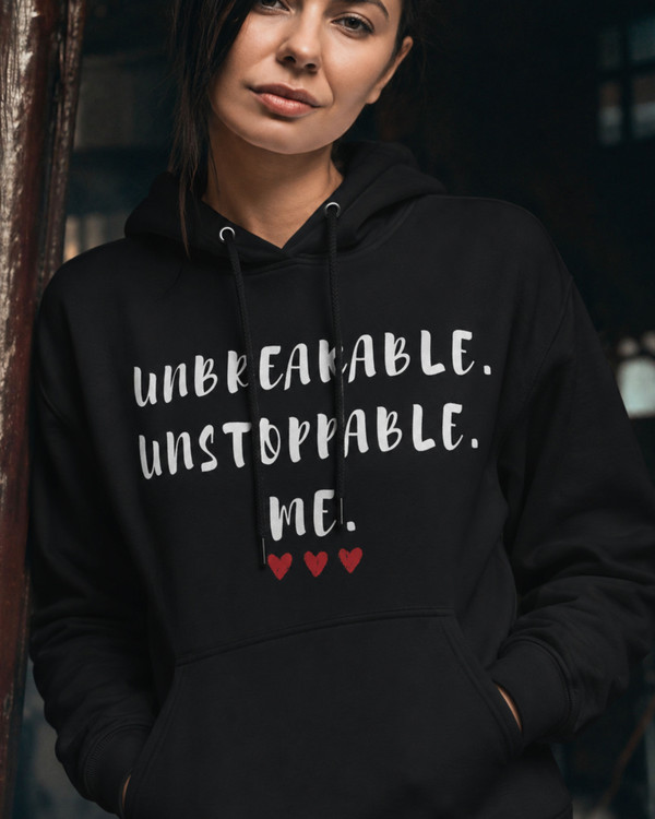 Woman wearing a black hoodie featuring the inspirational quote “Unbreakable. Unstoppable. Me.” with red heart accents, motivational apparel designed to inspire confidence, strength, resilience, and self-empowerment.