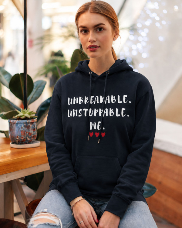 Woman wearing a navy blue hoodie featuring the motivational quote “Unbreakable. Unstoppable. Me.” with red heart accents, inspirational apparel promoting confidence, resilience, determination, and personal empowerment.
