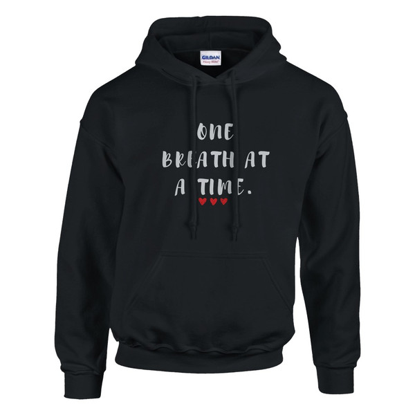 Black pullover hoodie featuring the inspirational quote “One Breath at a Time” with red heart accents, motivational unisex sweatshirt design promoting mindfulness, resilience, self-care, emotional wellness, and inner strength.