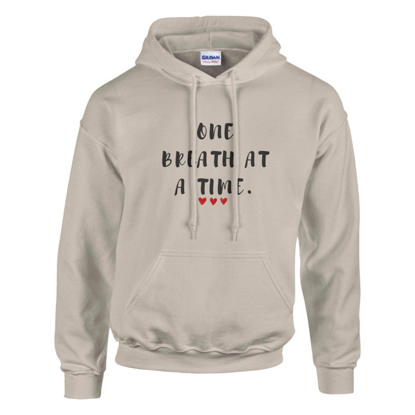 Beige pullover hoodie featuring the inspirational quote “One Breath at a Time” with red heart accents, motivational unisex sweatshirt design promoting mindfulness, resilience, self-care, emotional wellness, and inner strength.