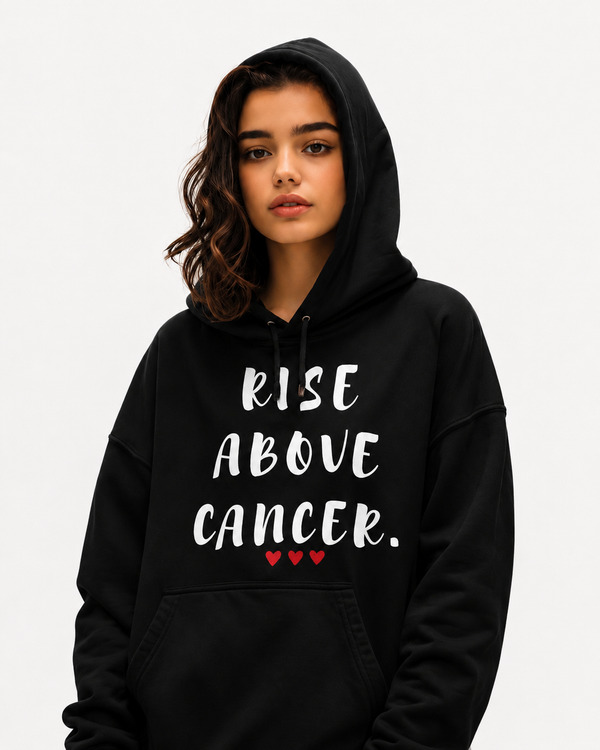 Woman wearing a navy blue hoodie featuring the inspirational quote “Rise Above Cancer” with red heart accents, motivational apparel promoting strength, hope, courage, and cancer awareness in a casual setting.