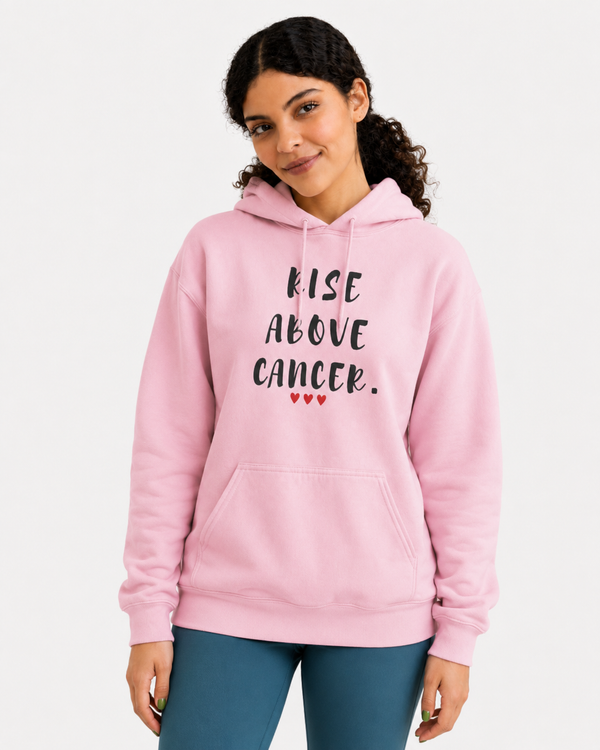 Woman wearing a pink hoodie featuring the inspirational quote “Rise Above Cancer” with red heart accents, taking a selfie while holding a small dog, motivational apparel promoting hope, strength, resilience, and cancer awareness.