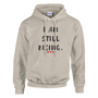 Front view of a sand-colored hoodie featuring the inspirational “I AM STILL RISING” design with three red heart accents. Motivational apparel promoting resilience, strength, perseverance, healing, and personal growth.