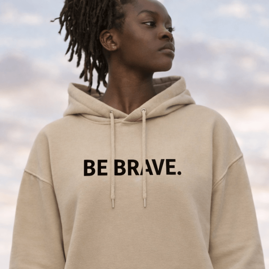 Multicolored woman wearing sand coloured hoodie with BE BRAVE. quote