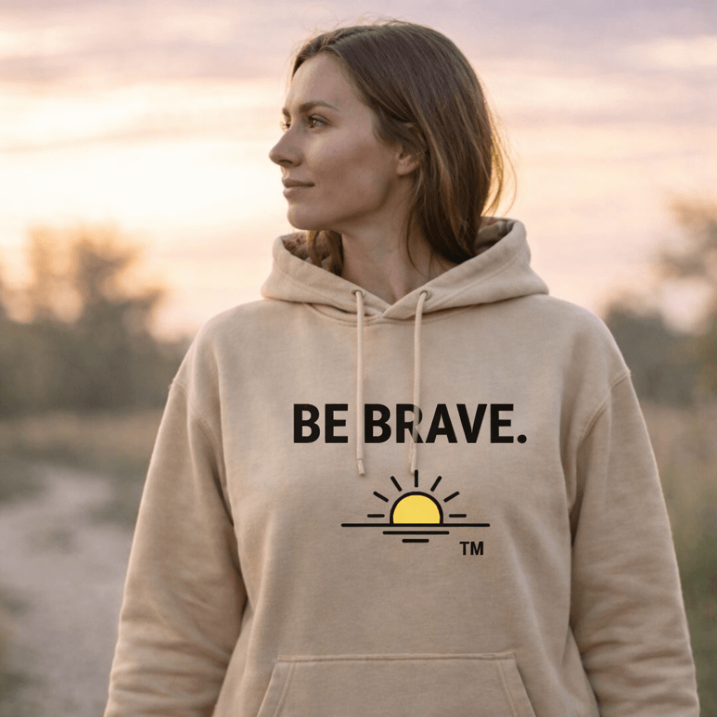 #Young woman looing to her right sunset behind her. sand coloured hoodie, BE BRAVE. and sunrise logo