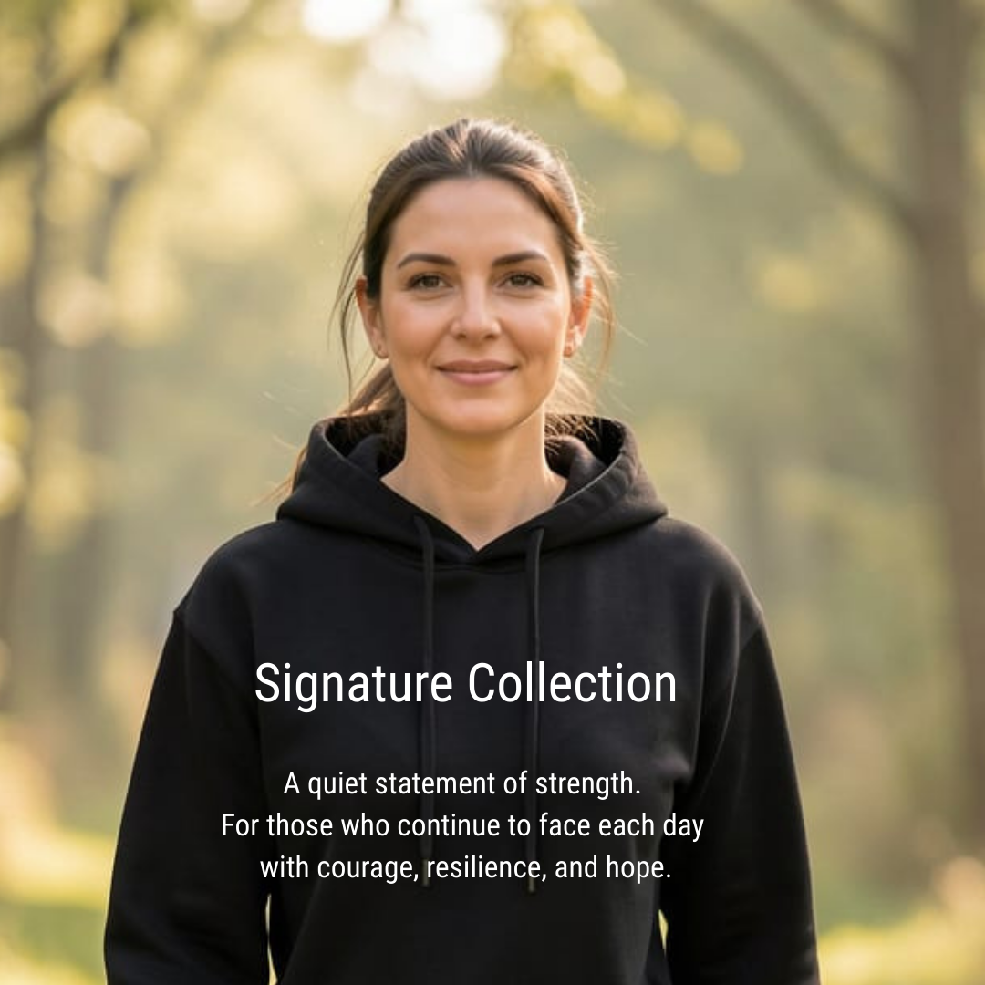 he image features a medium shot of a woman with medium-length brown hair pulled back in a ponytail. She is wearing a black hoodie and looking directly at the camera with a gentle, warm smile. Her skin tone is fair to medium.  The scene is outdoors, with a blurred background of greenery and trees, suggesting a park or natural setting. The lighting is soft and diffused, with a warm, golden hue, possibly indicating late afternoon or early morning light. The background is out of focus, creating a shallow depth of field that makes the woman stand out as the primary subject.  Overlaid on the lower portion of the image is text. The main heading reads "Signature Collection" in a clean, white sans-serif font. Below this, a smaller block of text provides a descriptive message: "A quiet statement of strength. For those who continue to face each day with courage, resilience, and hope." This text reinforces the overall mood of the image, which conveys a sense of understated power and optimism.  The visual effect of the image is calm, inviting, and inspiring. The soft lighting and natural setting contribute to a peaceful atmosphere, while the woman's expression and the accompanying text create a feeling of empowerment and encouragement. The composition effectively draws attention to the woman and the message, making it suitable for use in marketing or motivational contexts.