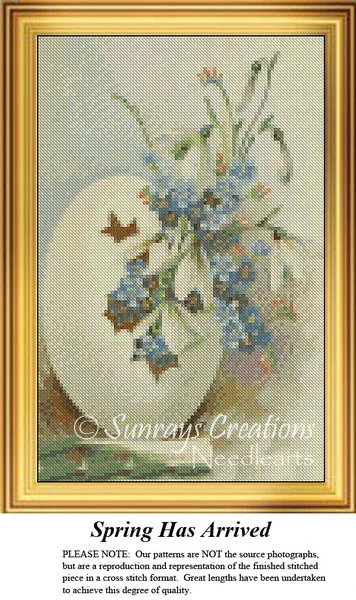 A large white egg with a brown bird design holds a sprig of blue flowers, created as a counted cross stitch pattern.