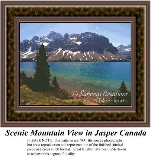 A scenic mountain view with bluish green waters in front of snow-streaked peaks and tall pine trees, suitable for a cross stitch project.