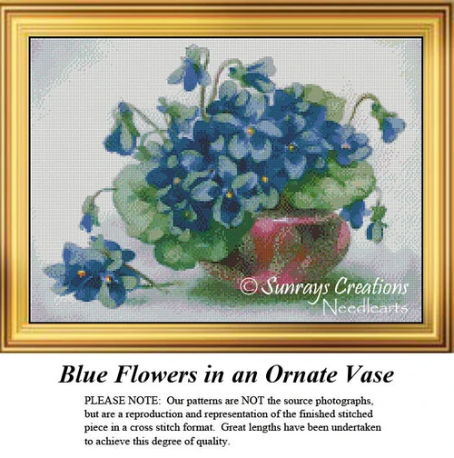 A bouquet of blue flowers with yellow centers spills over a mauve vase, immortalized as a counted cross stitch pattern.